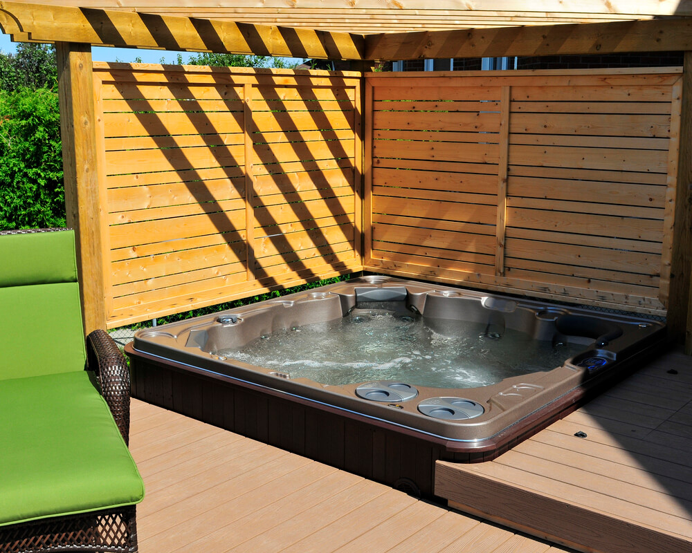 hot tub in a backyard with a wooden deck and a privacy fence