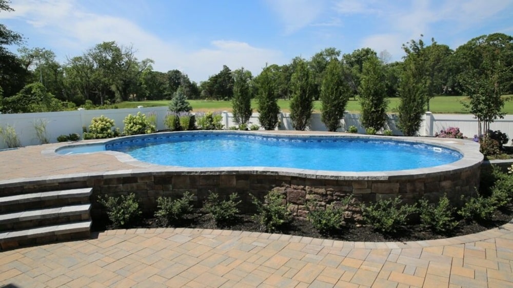 semi In-Ground Swimming Pool with Stone Patio and Lush Green Landscaping